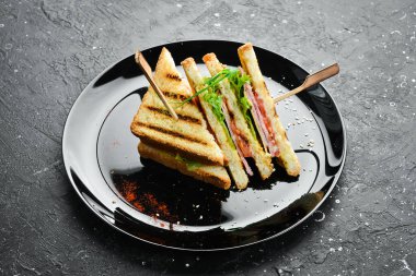 Pastırmalı sandviç, peynirli, domatesli ve marullu. Fast food. Siyah bir tabakta. Kırsal biçim.