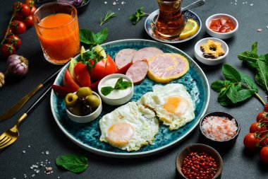 İngiliz kahvaltısı. Kızarmış yumurta, salam, pastırma ve sebze. Çay ve tatlı. Koyu bir arkaplanda.