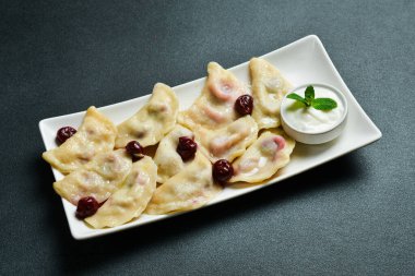 Beyaz kare tabakta vişneli ve ekşi kremalı hamur tatlısı. Metin için boş alan. Karanlık bir arka planda.