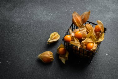 Taze altın sulu kış kirazları, siyah taş bir masanın üzerinde bektaşi üzümü (physalis). Kapat..