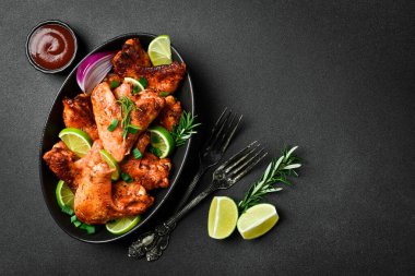 Limonlu, biberiyeli ve soğanlı kızarmış tavuk kanadı. Siyah bir tabakta. Karanlık bir arka planda.