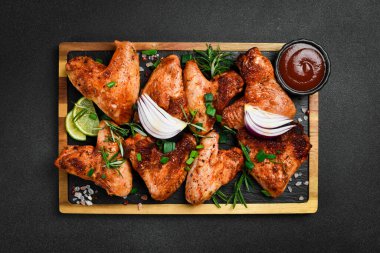 Tahtada soğan ve baharatla kızarmış tavuk kanadı. Karanlık bir arka planda.