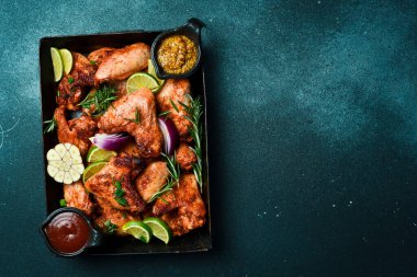 Izgara menüsü, barbekü. Metal bir tepside fırında tavuk kanadı. Karanlık bir arka planda.