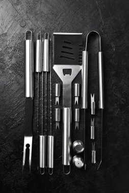 Çelik barbekü ve ızgara seti. Siyah bir tahta üzerinde. Üst görünüm.