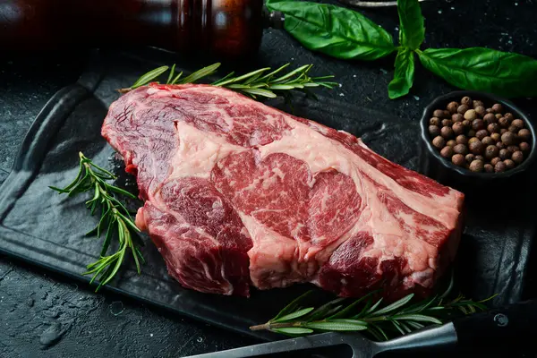 Siyah taşlı arka planda çatalı olan çiğ biftekli siyah Angus. Kırsal biçim.