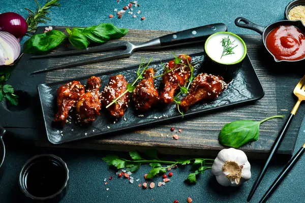 Bal soslu tavuk kanadı ve siyah taş tabakta susam tohumu. Karanlık bir arkaplanda, yakın plan.