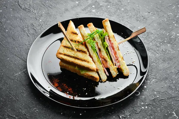 Pastırmalı sandviç, peynirli, domatesli ve marullu. Fast food. Siyah bir tabakta. Kırsal biçim.