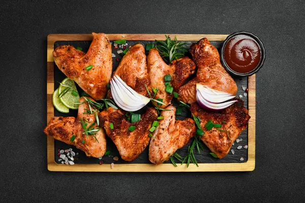 Tahtada soğan ve baharatla kızarmış tavuk kanadı. Karanlık bir arka planda.