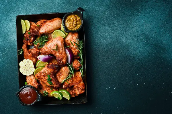 Izgara menüsü, barbekü. Metal bir tepside fırında tavuk kanadı. Karanlık bir arka planda.