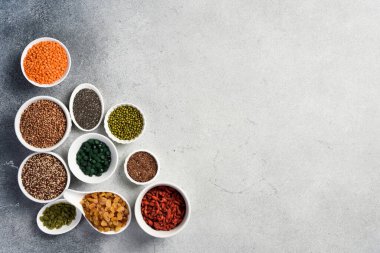 Süper yiyecekler, tahıllar, fındıklar ve kuru meyveler beyaz seramik kaselerde. Beyaz bir taş masanın üzerinde..