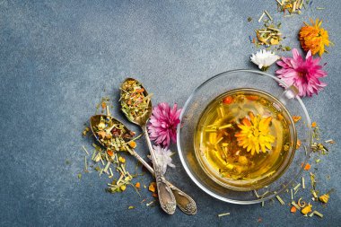 Sağlıklı bir fincan bitki çayı, kuru çay ve çiçekli kompozisyon. Gri beton arka planda. Dikey fotoğraf.