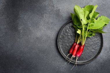 Siyah taştan bir tabakta taze organik kırmızı turp. Karanlık bir taş arka planda.