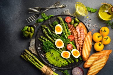 Lezzetli bir kahvaltı. Güneşli tarafı yumurta, kuşkonmaz, pastırma ve avokado. Siyah taştan bir tabakta.