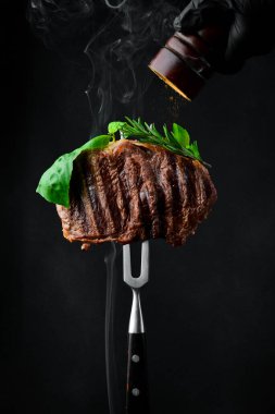 Biber değirmenli çatallı biftek, fotoğrafta donmuş karabiber parçacıkları. Izgara biftek. Siyah bir arkaplanda.
