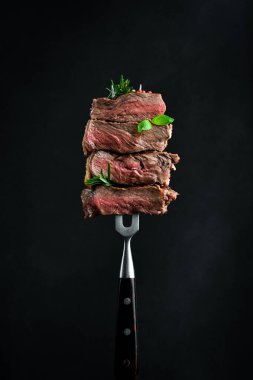 Metal bir çatalla pirzola bifteği dilimleri. Az pişmiş rosto. Siyah bir arkaplanda.