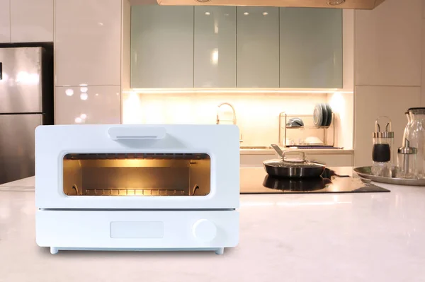 white modern design toaster oven is on the white marble table with background of nice dinner kitchen room during breakfast