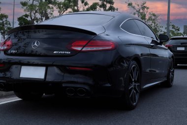 Güzel tasarlanmış arka lamba ve siyah spor araba markası Mercedes Benz c200 AMG Coupe Parkı 'nın arka kanat spikeri tren istasyonunun yakınındaki alacakaranlık gökyüzünün arka planına sahip.