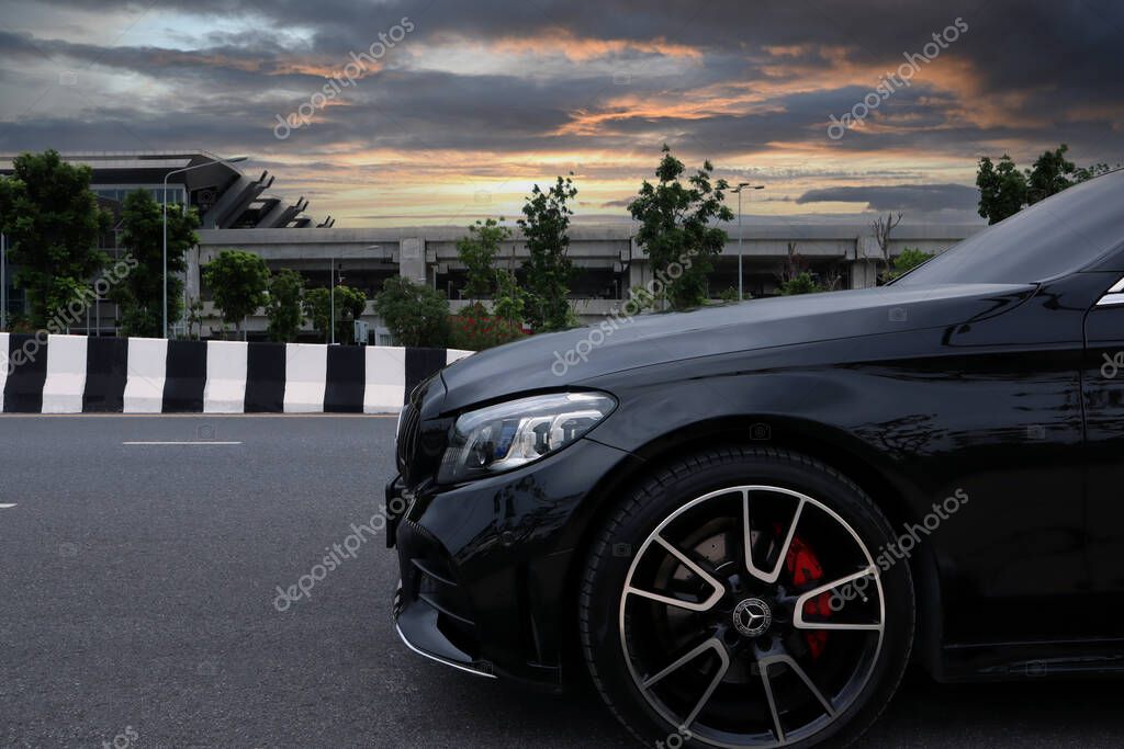 Led headlight and front left wheel of luxury black color Mercedes Benz sports car, c class c200 coupe AMG model park on road in evening near train station during trip