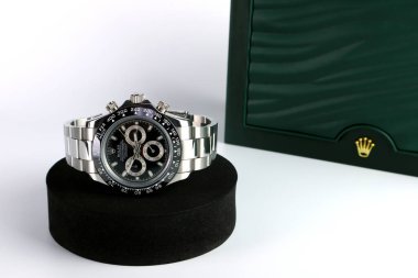 Rolex wristwatch model daytona oyster perpetual with black ceramic bezel stainless steel body displayed on white table with Rolex signature green box in the authorized distributor shop clipart