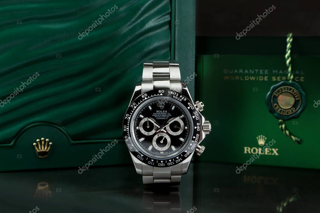 The Rolex vintage wristwatch ceramic bezel Cosmograph Daytona model display on mirror shelf table with background of Rolex green box crown logo , coin and manual and guarantee book in Rolex shop