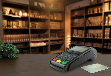 Kredi kartı okuyucu pos makinesi ve kredi kartı arka planı ev aromalı parfüm ürünleri perakende dükkanında olan ahşap masanın üzerinde.