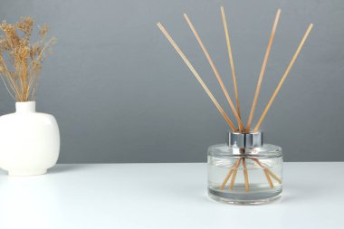 Lüks kokulu kamış aromalı cam şişesi romantik yaratmak ve yatak odasındaki ortam ortamını rahatlatmak için beyaz masanın üzerindedir. Sevgililer Günü sabahında gri çimento duvar arka planında izole edilmiş.