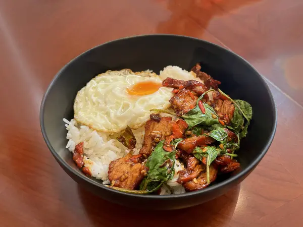 stir fried Thai basil with minced pork and chilli on topped rice , Thai local food style Thai food stir-fried chicken spicy and Basil served with rice ,fried egg and tomato cucumber carved black plate