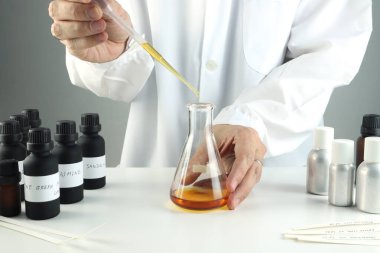 chemical beaker , flask is on white table with blotting paper , fragrance bottle and essential oil bottle are used to blend the nice scent for making perfume and candle by perfumer in the laboratory