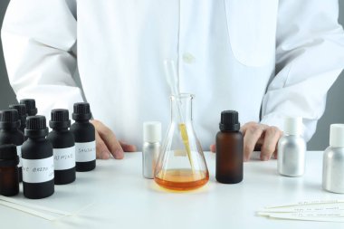 Kimyasal deney şişesi, beyaz masanın üzerinde leke, parfüm şişesi ve parfüm yapımında kullanılan esaslı kokuyu laboratuvardaki parfüm dağıtıcısıyla karıştırmak için kullanılıyor.