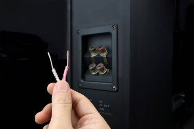 left hand of sound engineer holding speaker cable or audio cables for connecting big black surround speakers in a luxury home entertainment theater room of modern house during sound checking process clipart