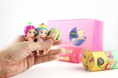 cute art toys blind box , Sonny Angel from dreaming , sweeties , and harvest series are in left hand  with background of nice design package box with white cement wall background in toy shop clipart