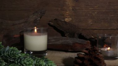 Yeni yıl kutlamaları sırasında rahatlamak için oturma odasındaki eski ahşap kulübe duvarının arka planında bulunan ahşap masa üzerinde lüks kokulu mum camı yakmak.