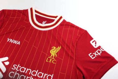 Liverpool futbol takımının güzel kırmızı futbol forması ya da spor tişörtü İngiliz Premier Ligi 'nde, kulüp logosu ve beyaz masa üzerinde Standart Chartered logosu olan, 2025 Şampiyonlar Ligi Premier Ligi