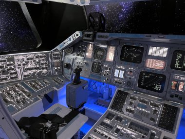 birçok kontrol düğmesi ve uzay gemisi kokpit kontrol paneli ve astronotlar arka planı yıldızlarla dolu pilot koltukları kamu uzay araçları sergisinde sergileniyor.