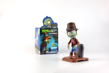 Zombi oyuncağı, bitkilerin zombilere karşı oynadığı ünlü video oyunu serisinden güzel tasarlanmış gizemli kutu paketi ve oyuncak mağazasındaki beyaz beton duvarla beyaz masa raflarında çekici bir görüntü.