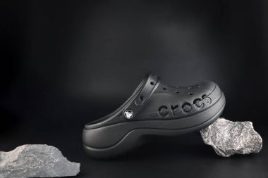 Siyah Crocs ayakkabıları siyah zeminde sergileniyor. Arka planda taşlar var. Ayakkabı mağazasında timsah yaşam tarzı sandaletler giyiyorlar.