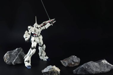 Gundam Plastik Model Kitleri veya Gundam Model Tekboynuz Gundam ölçekli Japon animasyon sedlerinden toplanan Gundam modeli siyah arkaplanda taşlarla siyah masada bulunmaktadır.