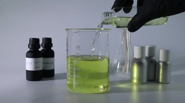 Eldeki pipet, parfüm ve mumu karıştırmak için kullanılıyor. Laboratuvarda parfüm yapımında kullanılıyor. Kağıt şeritlerin arkaplanı, parfüm şişesi ve beyaz masa üzerinde gerekli yağ şişesi.