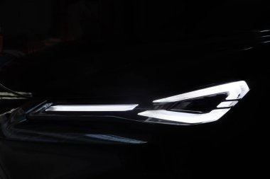 Chang An Deepal 005 elektrikli aracının ön far tasarımını kapat. Aydınlatılmış beyaz ışıklar, bu fütüristik EV 'nin modern tasarımı olan keskin tasarımı vurguluyor. Çin 'de karanlık bir garajda yakalandı.