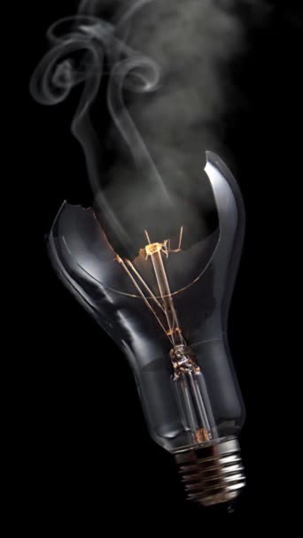 垂直断电灯泡吸烟4K回路的特点是 一个破碎的灯泡与一个黑色背景相对照 烟在垂直比例回路中旋转 — 图库视频影像