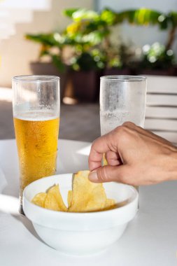 Beyaz bir masanın üzerinde elinde bir patates cipsi ve arkasında da bira bardakları vardı. Tenerife. Kanarya Adaları. İspanya