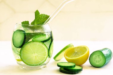 Bardakta samanla taze soğuk yaz içkisi. Dilimlenmiş limonata, limon, salatalık, nane ve parlak sarı arka planda buz. Kapatın. Seçici odaklanma. Bulanık arkaplan.