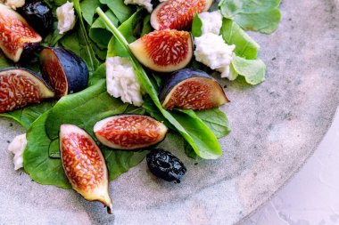 Yakın plan sağlıklı yaz salatası, incir, beyaz peynir, roka, gri seramik tabakta siyah zeytin. Sağlıklı yeme kavramı.