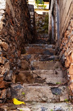 Old rock staircase with city view on background. Abandoned narrow stairway in the town. Selective focus. Blurred background.
