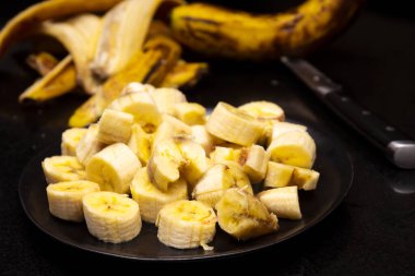 Muz tabakta dilimler. Siyah arka planda olgunlaşmış organik tatlı meyve. Karanlık, sade anahtar. Doğal sağlıklı atıştırmalıklar. Seçici odaklanma. Bulanık arkaplan.