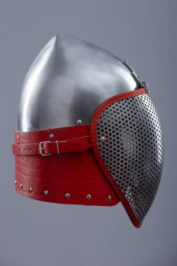 Koruyucu ağ vizörlü modern eskrim kaskı. Parlak gümüş bir miğfer tam bir yüz kafesi içerir ve kırmızı deri kayış ve metal tokayla güvence altına alınır..