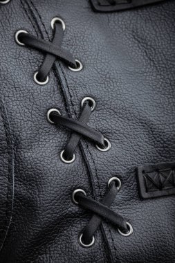 Siyah Deri Ceket Bağlama 'nın yakın çekimi. Bu resim siyah deri kolsuz ceketin yanındaki dekoratif bağlama detaylarının yakın çekimini gösteriyor. Siyah bağcıklar gümüş göz bebeklerinden geçirilir ve çapraz çapraz desen oluşturur..