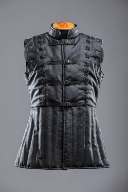Dantelli ve kalçalı siyah deri kolsuz ceket. Bu resim siyah, kolsuz bir ceket ya da yüksek yakalı bir yelek gösteriyor. Sergide dekoratif süsleme ayrıntıları ve önünde gümüş tokalar bulunan ayarlanabilir kayışlar yer alıyor..