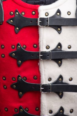 Kırmızı ve Beyaz Brigandine Zırh Detayları 'na yakın çekim. Bu görüntü, pirinç renkli çiviler, gümüş tokalı siyah deri kayışlar ve kırmızının zıt dokularını gösteren kırmızı ve beyaz brigandin zırhının detaylı bir yakın çekimini sağlar.