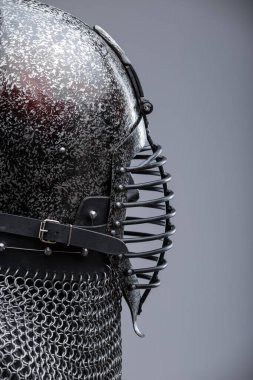 Ribbed Faceplaka ve Zincirli Kask. Bu görüntü koyu, muhtemelen karartılmış bir çeliği, sivri uçlu bir miğferi ve yatay kaburgaları olan belirgin bir yüz plakasını gösteriyor. Kaskın tabanından bir zincirli tasma uzanıyor..